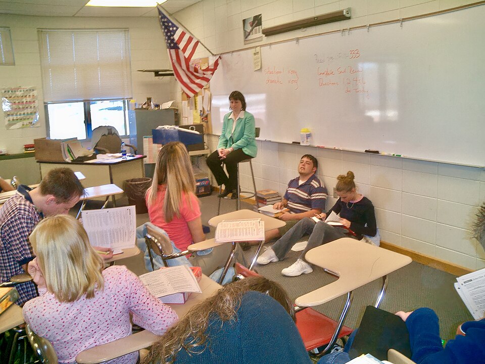 A teacher speaks with students seated in a high school classroom.